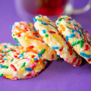 Colorful cookies with sprinkles on purple background.